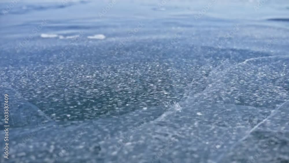 Snow is flying over surface of ice. Snowflakes fly on ice of Lake Baikal. Ice is very beautiful with unusual unique cracks. Snow sparkles and glows in red. Shooting slow motion 180fps. Picture at Snow is flying over surface of ice. Snowflakes fly on ice of Lake Baikal. Ice is very beautiful with unusual unique cracks. Snow sparkles and glows in red. Shooting slow motion 180fps. Picture at