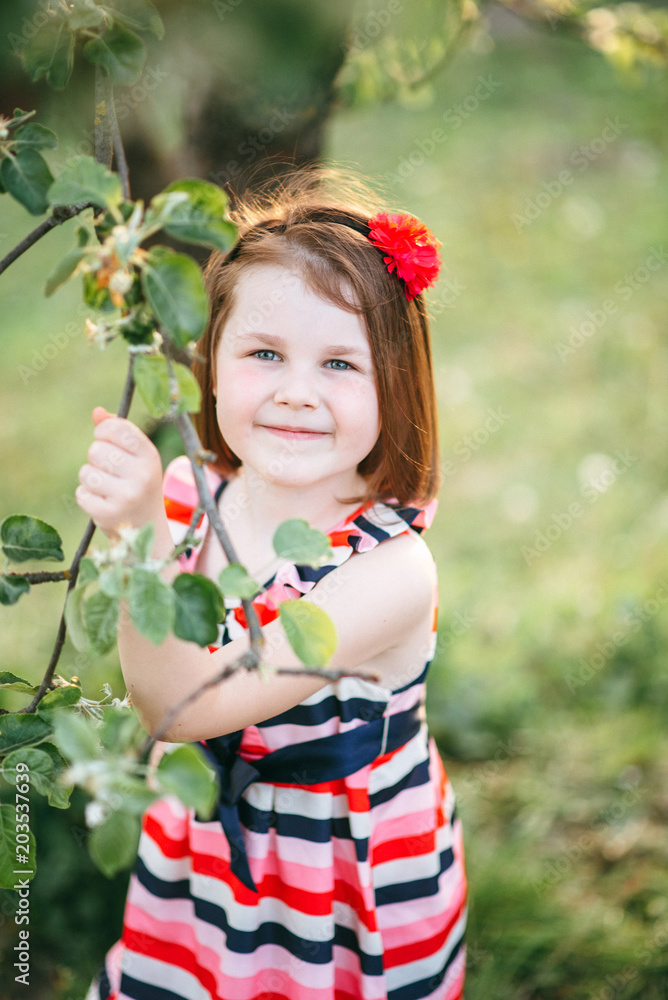 Portrait of a beautiful girl in a garden near a blossoming apple tree. Beautiful back light and happy baby in the garden Portrait of a beautiful girl in a garden near a blossoming apple tree. Beautiful back light and happy baby in the garden