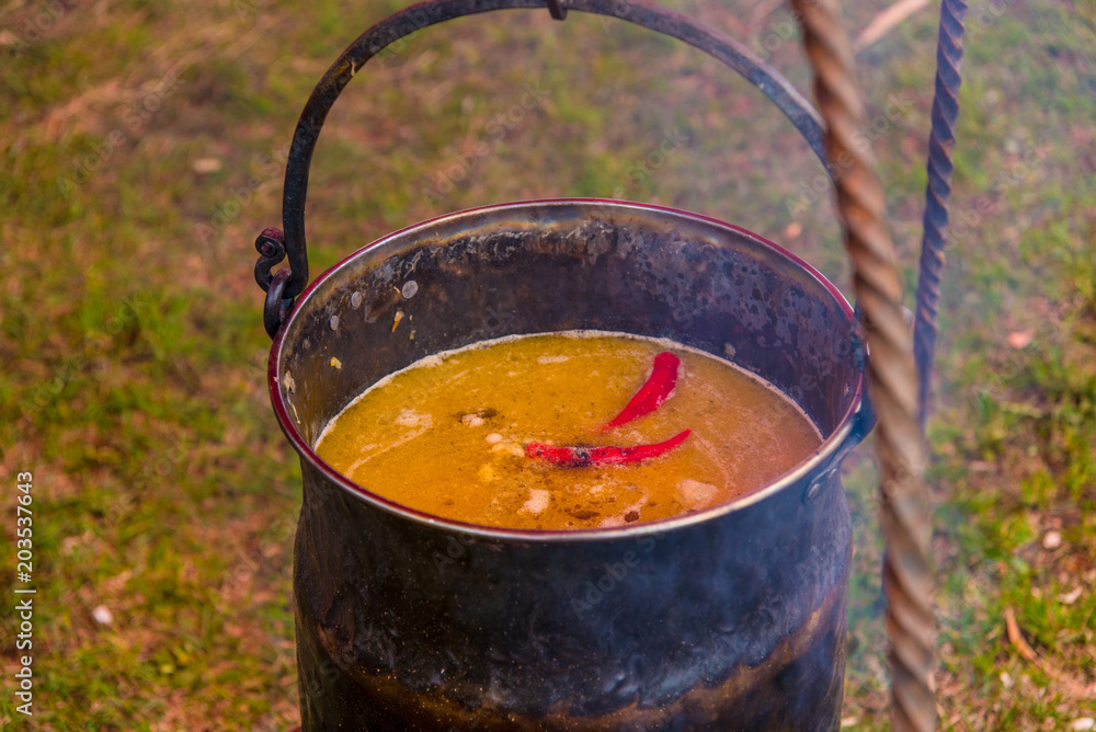 Soup with spicy pepper is cooked in a cauldron on an open fire Soup with spicy pepper is cooked in a cauldron on an open fire