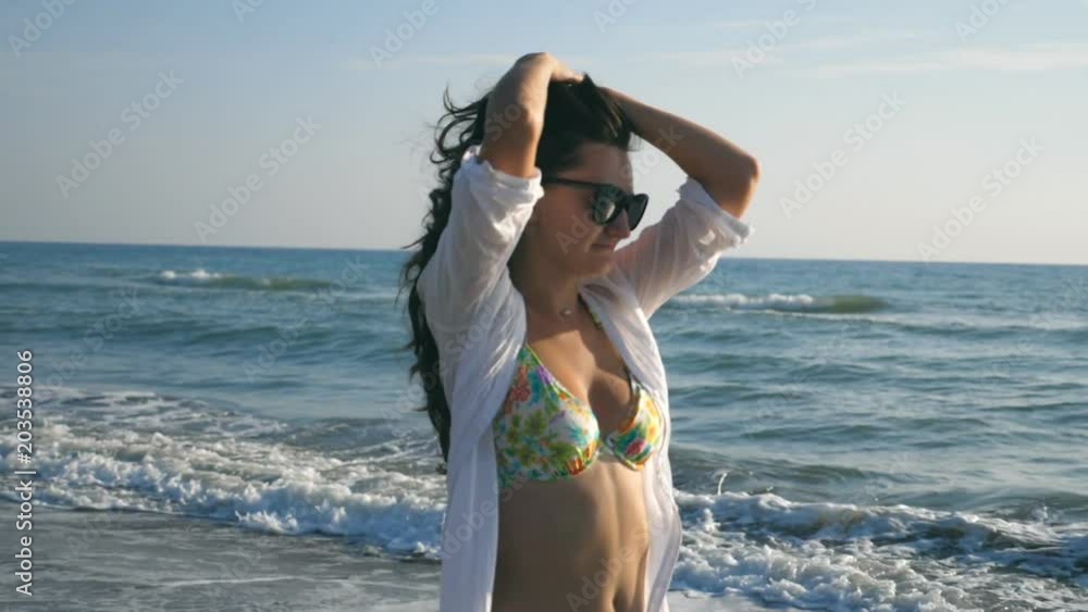 Happy woman walking and spinning on sea beach at sunny day. Young smiling girl in sunglasses playing with her hair and enjoying life during travel. Summer vacation or holiday. Slow motion Close up Happy woman walking and spinning on sea beach at sunny day. Young smiling girl in sunglasses playing with her hair and enjoying life during travel. Summer vacation or holiday. Slow motion Close up