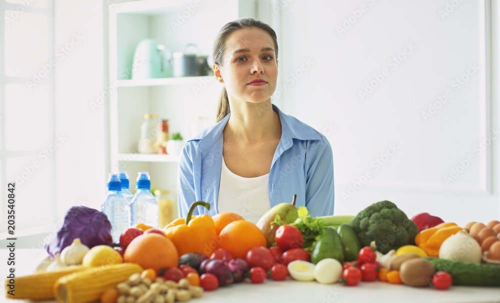 happy young housewife sitting in the kitchen preparing food from a pile of diverse fresh organic fruits and vegetables happy young housewife sitting in the kitchen preparing food from a pile of diverse fresh organic fruits and vegetables