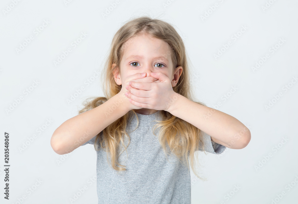 Silent, do not talk. Little girl covered her mouth with her hands on a light background. Silent, do not talk. Little girl covered her mouth with her hands on a light background.