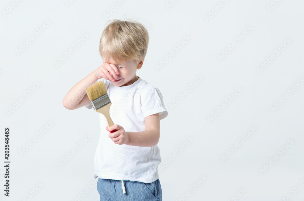 Crying little boy is holding a paintbrush in his hands. He cries and wants to paint. Crying little boy is holding a paintbrush in his hands. He cries and wants to paint.