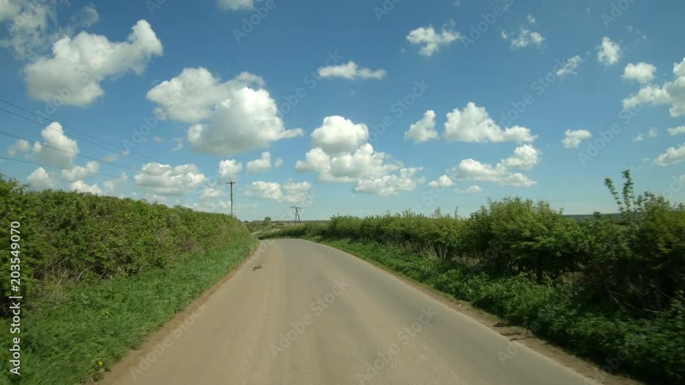Driving along a narrow twisting country road through the rolling english countryside in Northamptonshire in England. Vehicle POV.