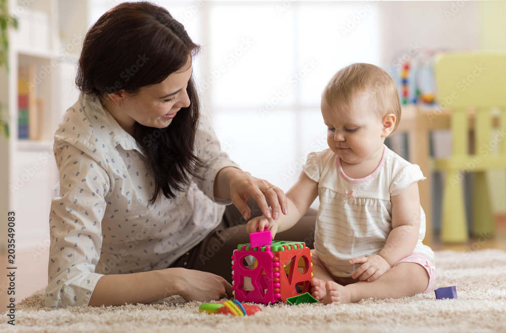 Fototapeta Opiekunka do dziecka i roczne dziecko bawiące się zabawkami w pokoju dziecinnym