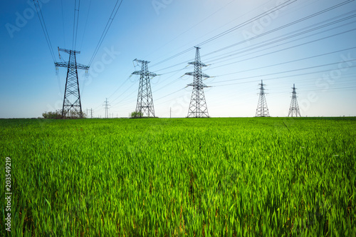 High voltage lines and power pylons in a green agricultural landscape with blue sky on a sunny day.