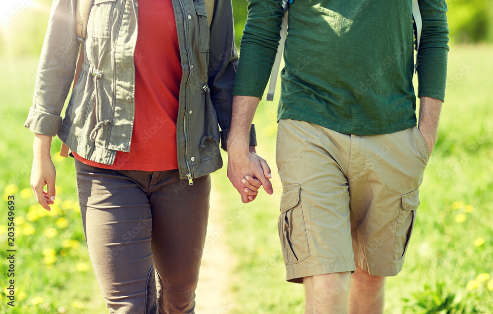 travel, hiking, backpacking, tourism and people concept - close up of couple with backpacks holding hands and walking along country road travel, hiking, backpacking, tourism and people concept - close up of couple with backpacks holding hands and walking along country road