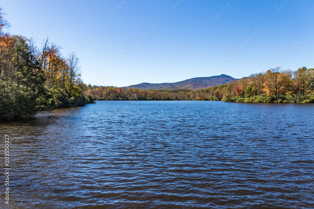 Autumn on a calm mountain lake surrounded by fall color and blue sky, and a mountain ridge line in the distance.