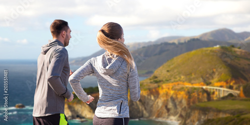 fitness, sport, people and healthy lifestyle concept - happy couple running over bixby creek bridge on big sur coast of california background