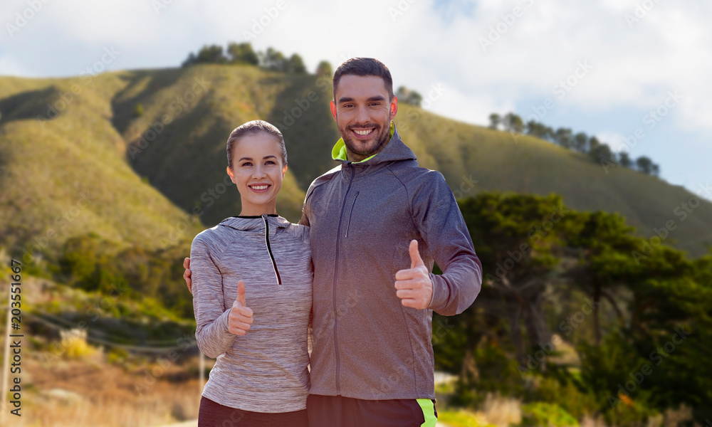 fitness, sport and gesture concept - smiling couple outdoors showing thumbs up over big sur hills background in california