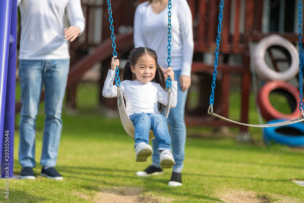 Happy daughter is enjoying to play with parents at park. Cute little girl having fun in playground with family. Happy daughter is enjoying to play with parents at park. Cute little girl having fun in playground with family.