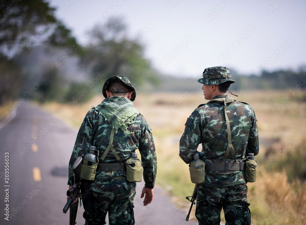 Asian army soldier return to base after completing military mission. Armed infantry walking in the foreground. Soldiers walking away on road concept. Asian army soldier return to base after completing military mission. Armed infantry walking in the foreground. Soldiers walking away on road concept.