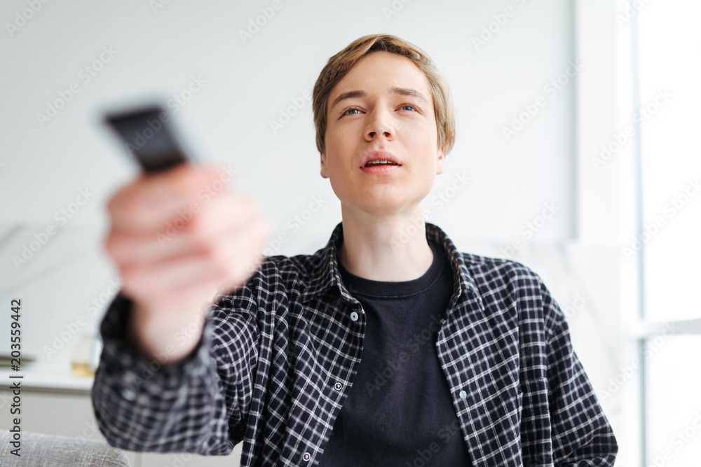 Portrait of young thoughtful man using a remote control while watching TV at home isolated Portrait of young thoughtful man using a remote control while watching TV at home isolated