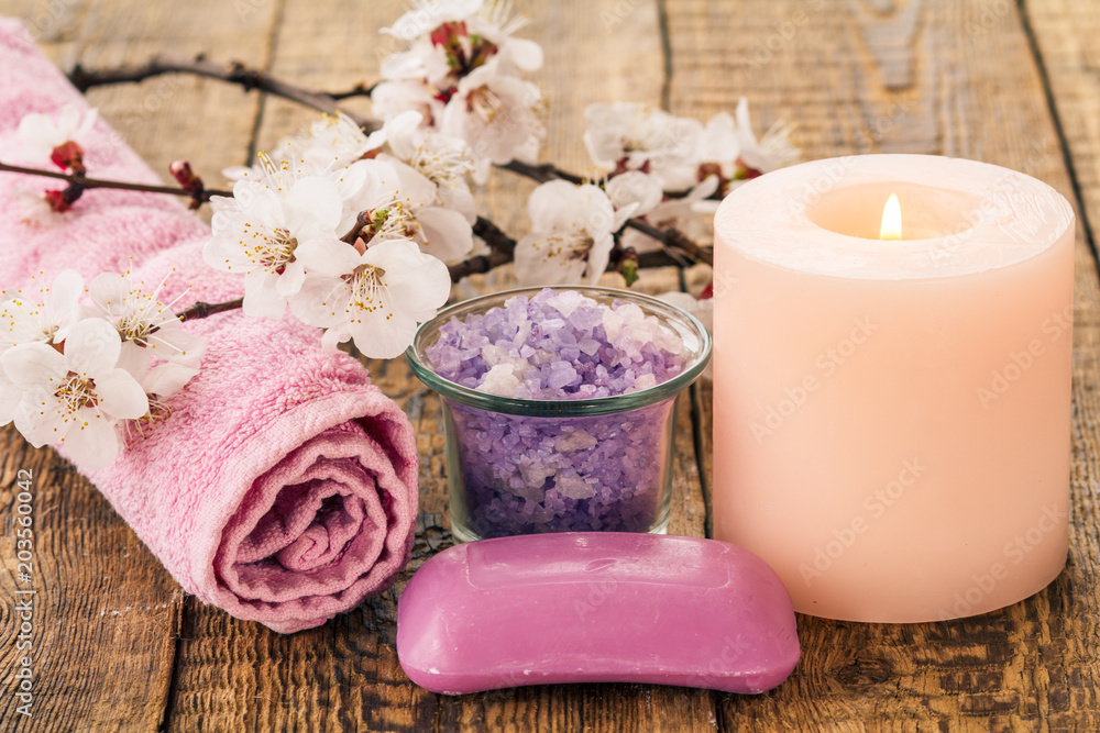 Soap, sea salt in glass bowl with towel for bathroom proceduresl and  burning candle with flowering branch of apricot tree