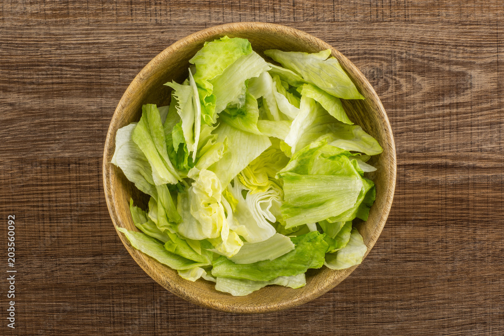 Iceberg lettuce table top fresh torn salad leaves in a wooden bowl isolated on brown wood background. Iceberg lettuce table top fresh torn salad leaves in a wooden bowl isolated on brown wood background.