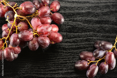 Two red globe grape clusters table top isolated on black wood background dark pink berries.