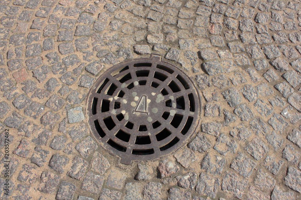 Manhole on Old Historical Cobblestone Street. Stone Textured Pavement and Manhole with Metal Cover on City Street. Manhole on Old Historical Cobblestone Street. Stone Textured Pavement and Manhole with Metal Cover on City Street.