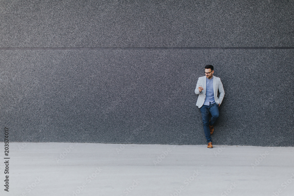 Young man standing by the wall witn mobile phone in the hand