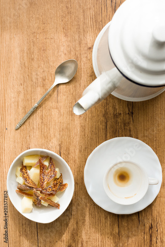 breakfast of slices of dried fig with pecorino cheese next to cup of coffee, teapot and spoon