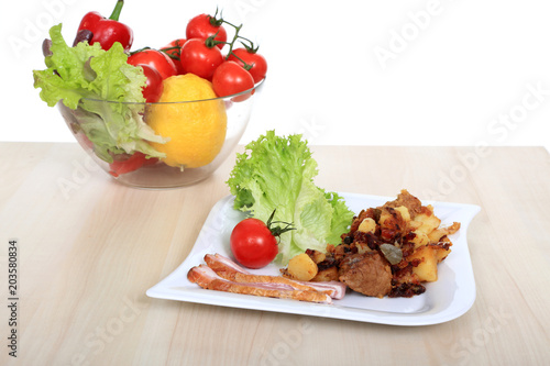 Mięso z ziemniakami i warzywami na białym kwadratowym talerzu.