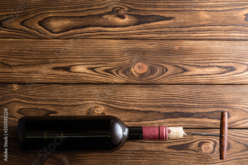 Bottle of red wine with corkscrew against wood