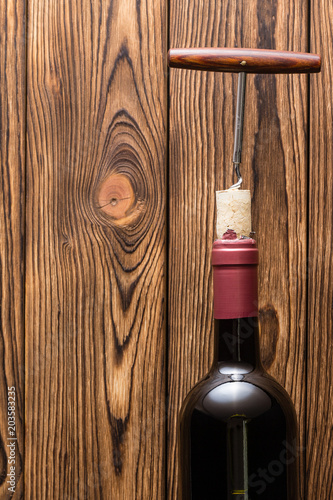 Bottle of red wine with corkscrew on wood