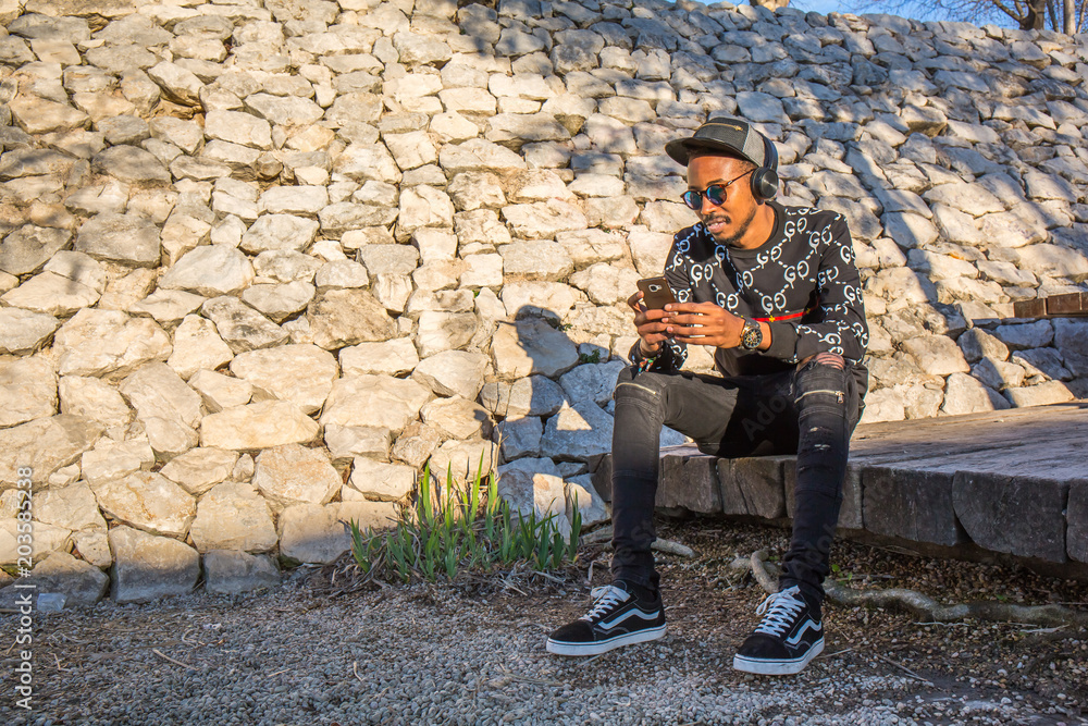 Fototapeta premium Black man in a park using the mobile phone and with headphones
