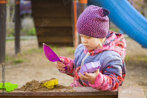 Маленькая девочка играет в песочнице.