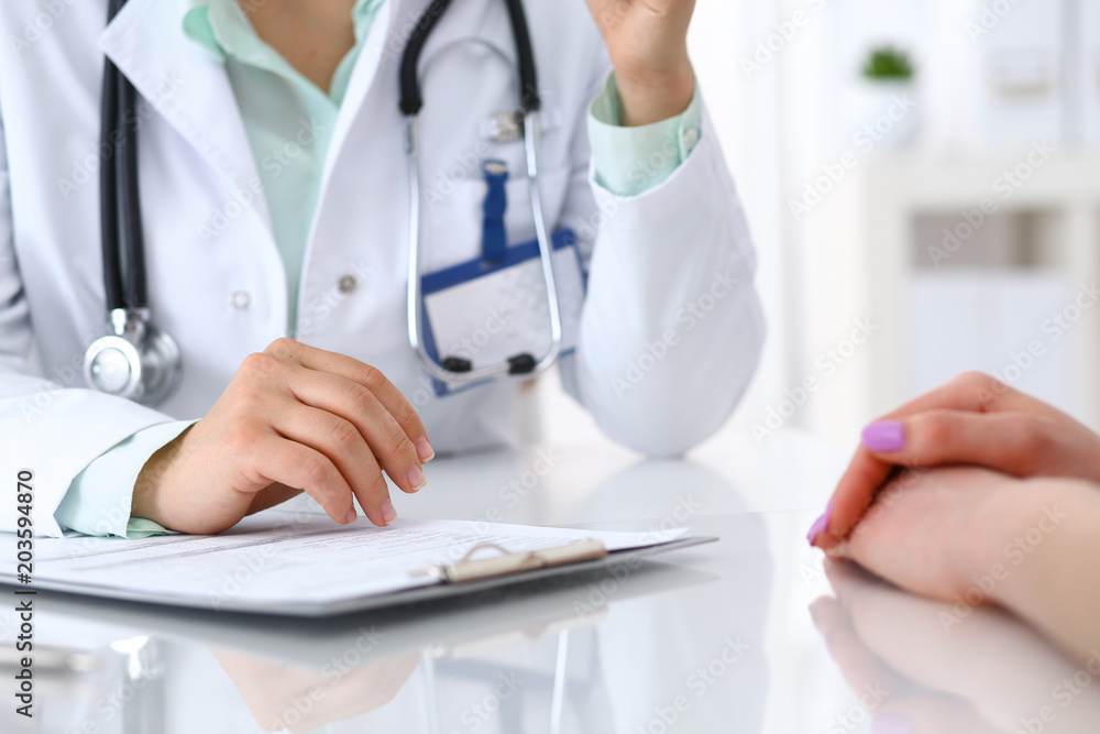 Doctor and patient talking while sitting at the desk in hospital office, closeup of human hands. Medicine and health care concept Doctor and patient talking while sitting at the desk in hospital office, closeup of human hands. Medicine and health care concept