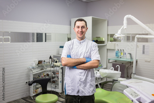 Male dentist standing with his hands crossed over medical office background. Healthcare  profession  stomatology and medicine concept