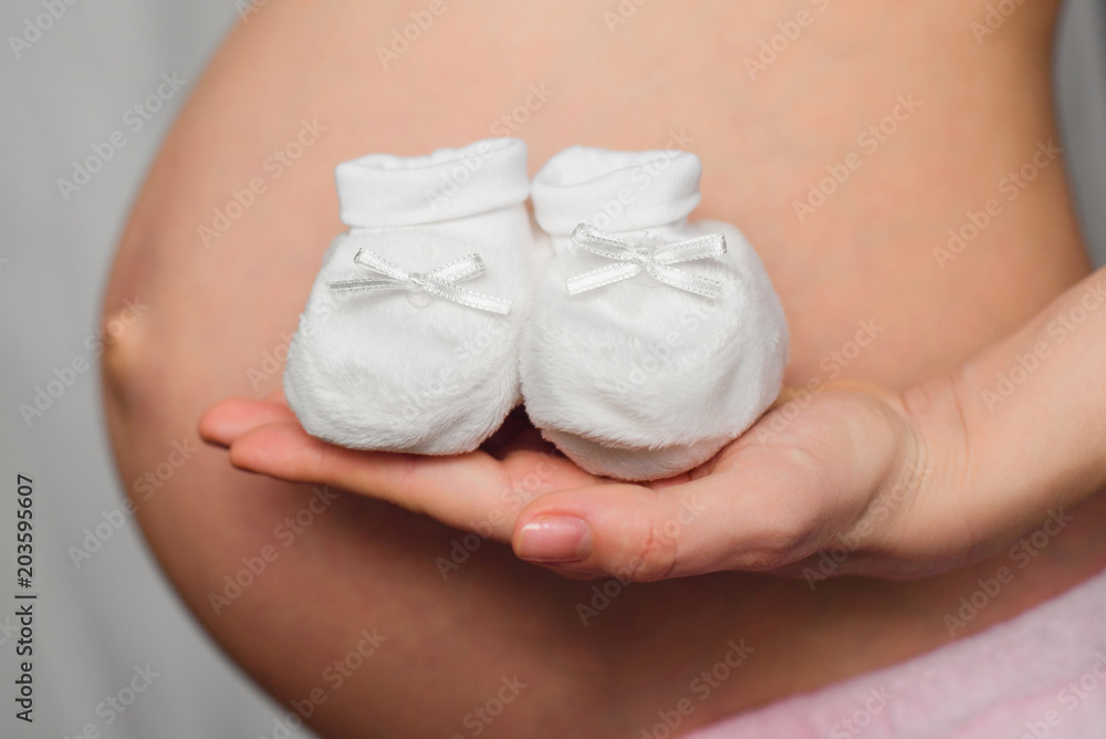 booties for newborn in the hands of a pregnant girl on the background of the abdomen booties for newborn in the hands of a pregnant girl on the background of the abdomen