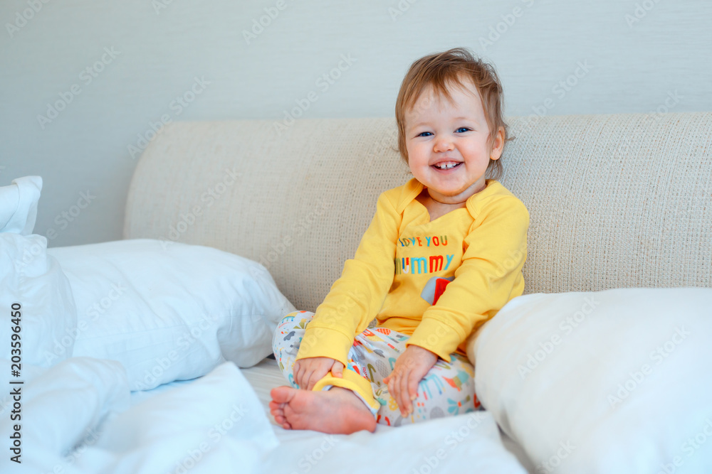 Funny little baby girl sitting in parents bed. Infant girl in yellow pajamas Funny little baby girl sitting in parents bed. Infant girl in yellow pajamas