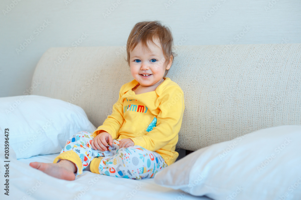 Funny little baby girl sitting in parents bed. Infant girl in yellow pajamas Funny little baby girl sitting in parents bed. Infant girl in yellow pajamas