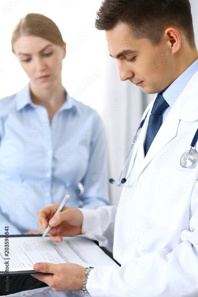Male doctor holding application form while consulting female patient in hospital office. Perfect service in medicine and healthcare concept Male doctor holding application form while consulting female patient in hospital office. Perfect service in medicine and healthcare concept