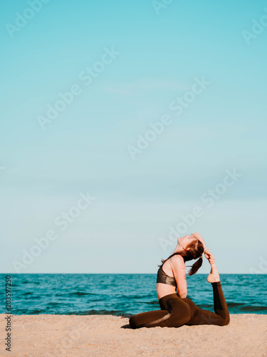 Young beautiful sporty woman in green clothing doing yoga asana on sea sandy beach near water. Girl practicing exercises. Health concept. Copy space. © kohanova1991