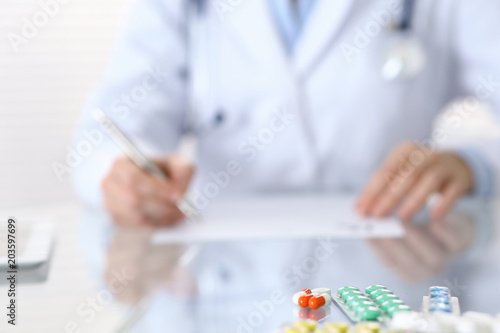Medicine pills closeup with doctor writing prescription form back in blur.  Healthcare, insurance and excellent service in medicine concept