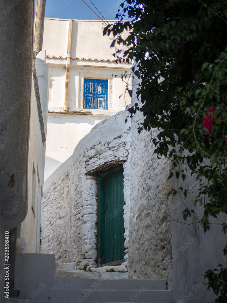 A narrow alley in Amorgos with its white stairs, a green door and a blue window