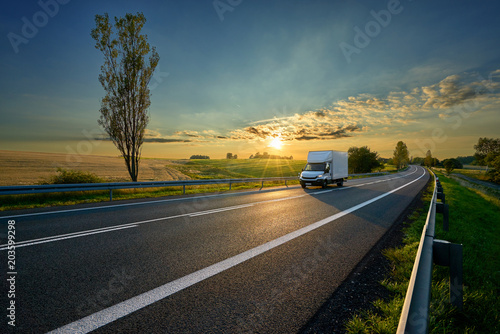 Obraz na płótnie White delivery van driving on asphalt road around farm fields in rural landscape at sunset w salonie