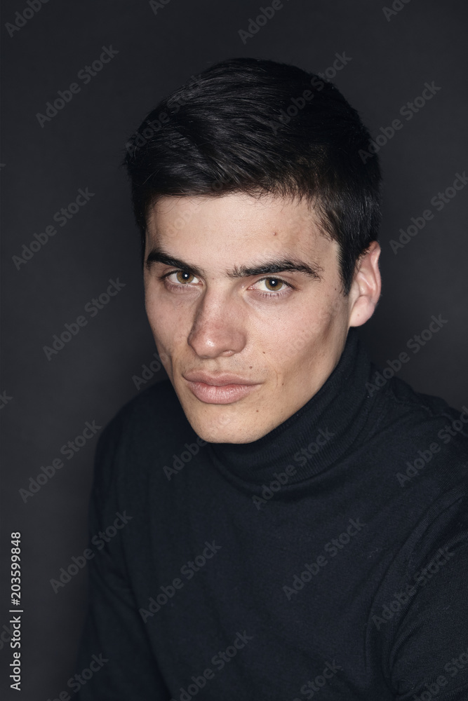 Naklejka premium jeden młody przystojny mężczyzna, model w golfie, prosty studyjny strzał górnej części ciała, czarne tło.