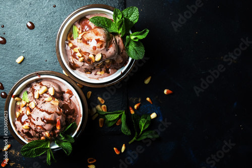 Chocolate ice cream with topping and fried pine nuts decorated with mint leaves, dark background, top view