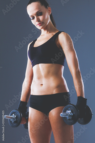 Muscular young woman standing on gray background. Muscular young woman