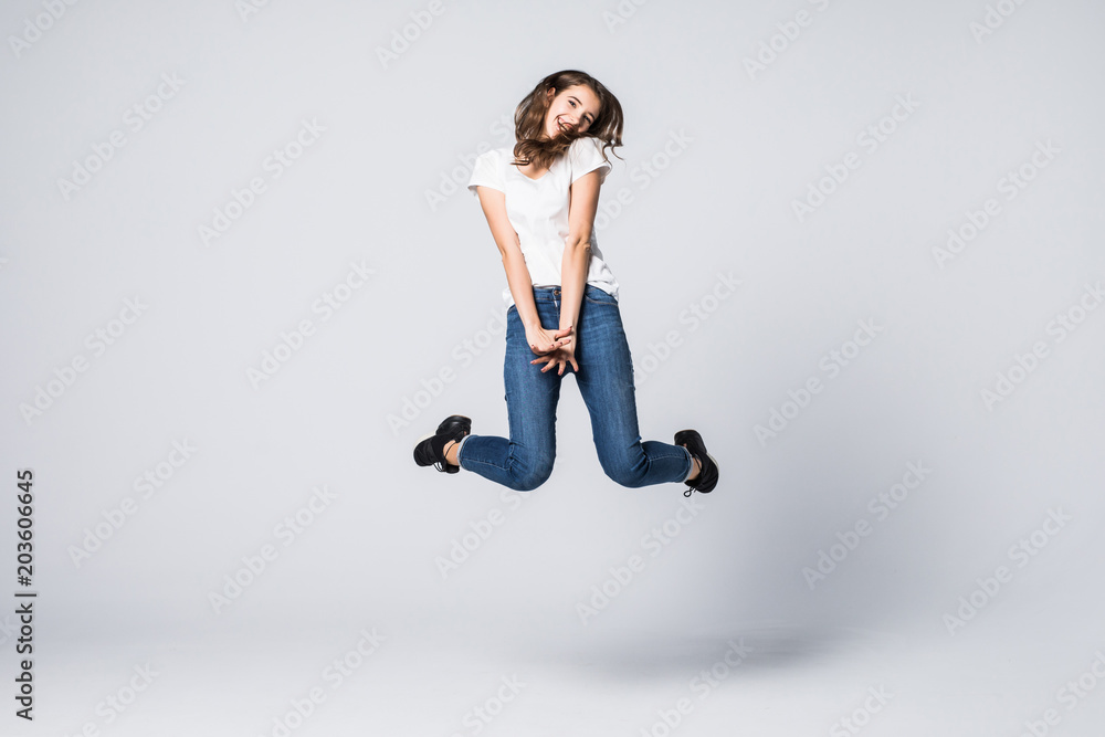 Smiling woman jumping in studio and looking at camera over gray background