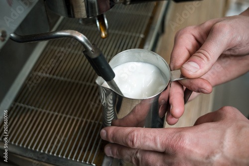 barista steaming milk before adding it to espresso to make cappuccino or latte. coffee bar equipment concept