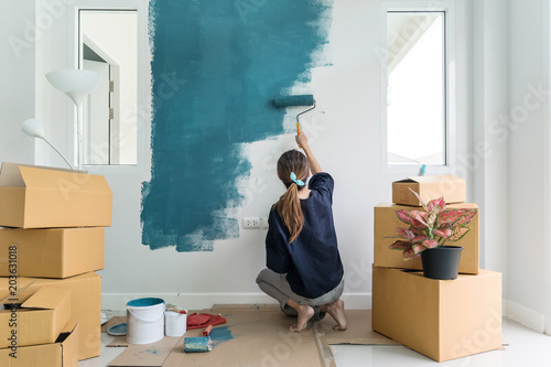Young asian happy woman painting interior wall with paint roller in new house, Home decoration concept