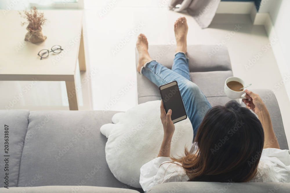 Young woman using smartphone at cozy home on sofa in living room - obrazy, fototapety, plakaty 