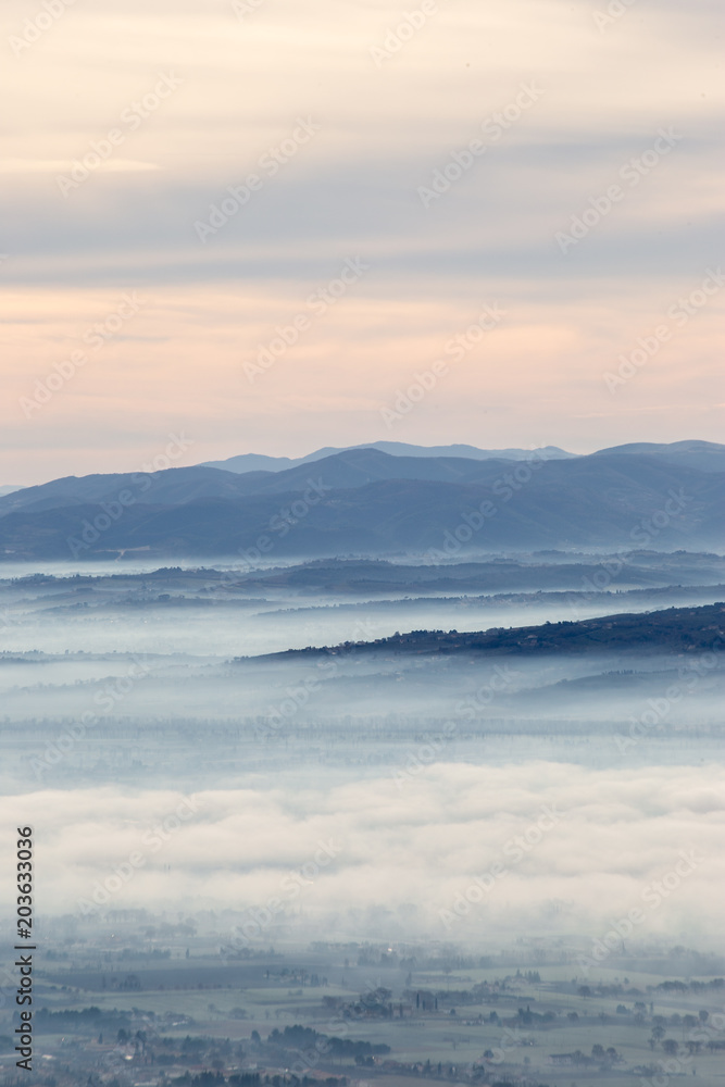 Fototapeta premium Beautiful aerial view of Umbria valley in a winter morning, with fog covering trees and houses