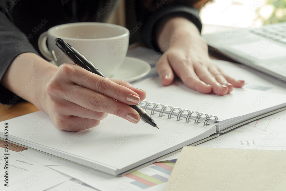business woman writing in book with a cup of coffee in office business woman writing in book with a cup of coffee in office