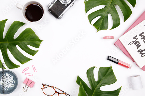 Women's home office desk workspace with tropical palm leaf, vintage camera, glasses, coffee cup, lipstick and notebook on white background. Flat lay, top view woman blog mock up. Creative concept.