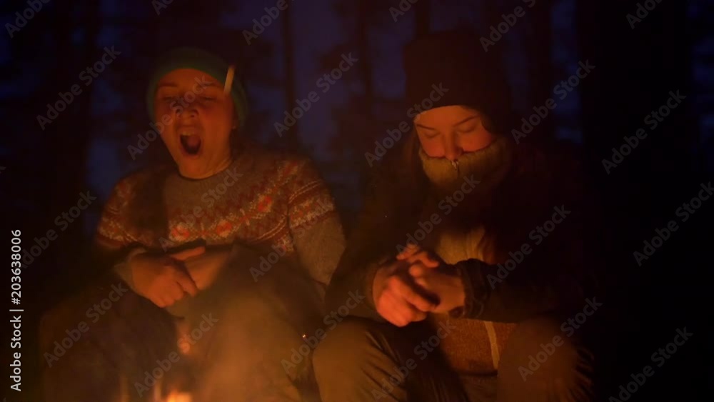 Young tired girls yawns sitting at the bonfire in the wood in the evening Young tired girls yawns sitting at the bonfire in the wood in the evening