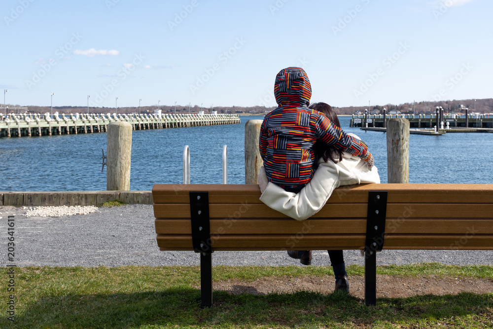 Mother and son sit on a wooden chair looking at the lake